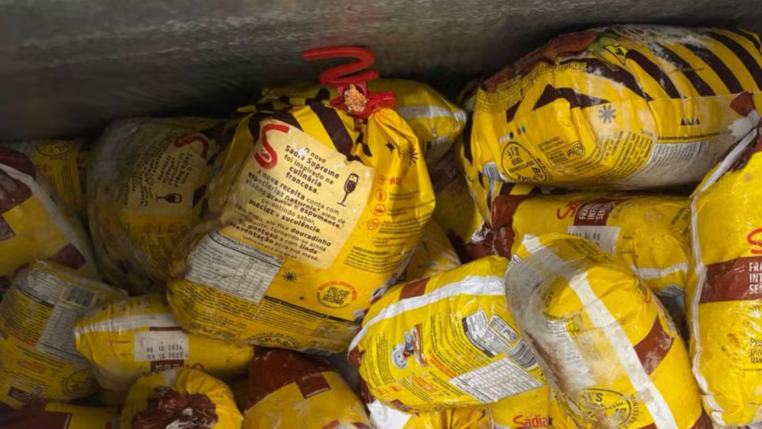 Diversos frangos congelados da marca Sadia embalados em sacos amarelos, empilhados dentro de um freezer industrial.