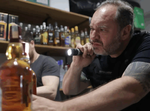 Policial aponta lanterna para uma bebida alcoólica