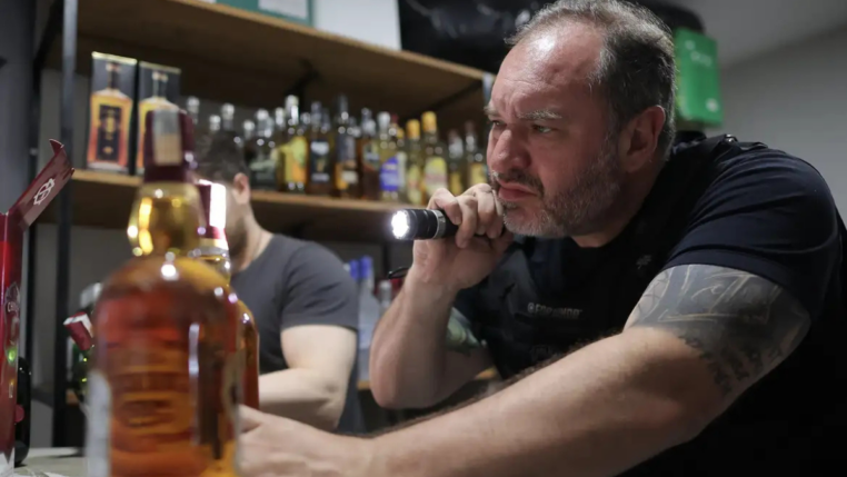 Policial aponta lanterna para uma bebida alcoólica