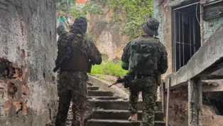 Policiais militares de costas, subindo uma escada, em uma comunidade.