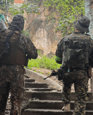 Policiais militares de costas, subindo uma escada, em uma comunidade.