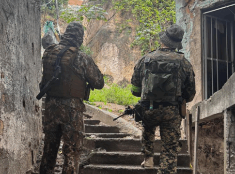 Policiais militares de costas, subindo uma escada, em uma comunidade.
