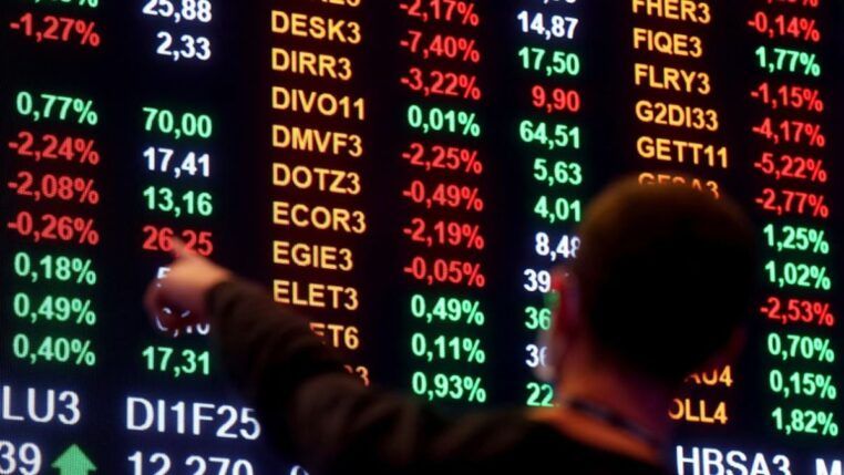 Homem aponta para números em painel da bolsa de valores