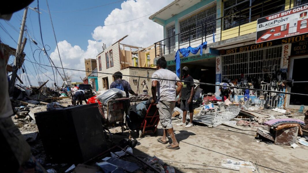 Homens empurram carrinhos com pertences em meio a rua destruída pelo furacão
