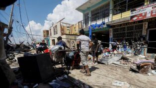Homens empurram carrinhos com pertences em meio a rua destruída pelo furacão