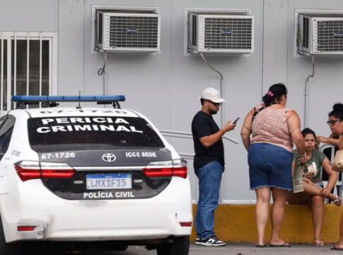Pessoas estão ao lado de um carro da Perícia Criminal à espera de informações no IML