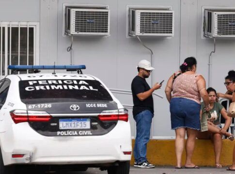Pessoas estão ao lado de um carro da Perícia Criminal à espera de informações no IML