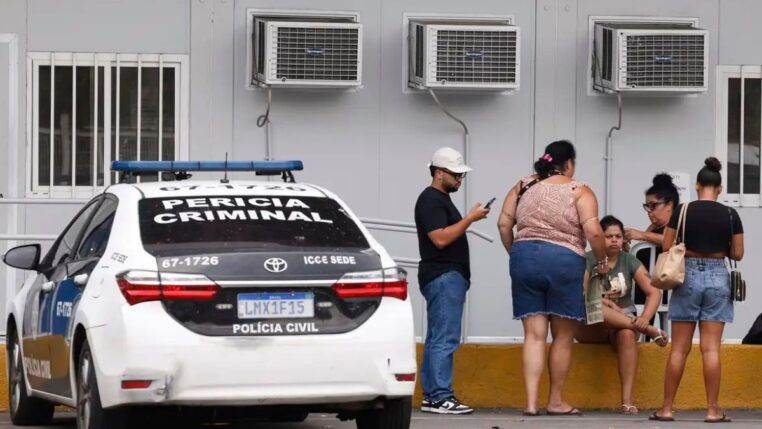 Pessoas estão ao lado de um carro da Perícia Criminal à espera de informações no IML