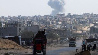 Trator carrega duas pessoas em estrada enquanto ao fundo uma fumaça grande aparece entre as casas