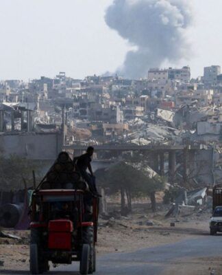 Trator carrega duas pessoas em estrada enquanto ao fundo uma fumaça grande aparece entre as casas