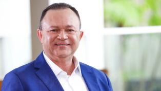 Carlos Brandão de roupa social, sorrindo e olhando para a câmera