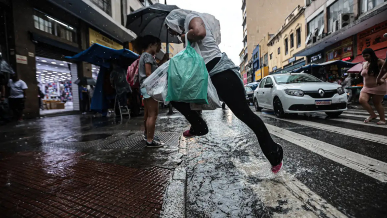 Imagem colorida de homem pulando uma poça d'água ao atravessar a rua