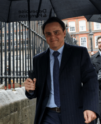 Felipe Massa veste terno e grava e segura um guarda-chuva caminhando pela calçada