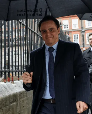 Felipe Massa veste terno e grava e segura um guarda-chuva caminhando pela calçada