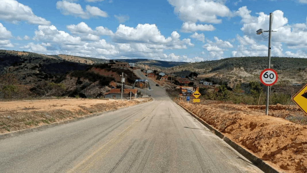 Radar de controle de velocidade instalado em rodovia de área rural, próximo a vegetação e montes, em um dia ensolarado.