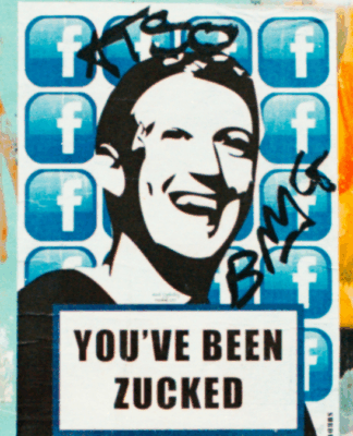 Em um parede com grafites, há um poster com uma ilustração do rosto de Mark Zuckenberg, CEO da Meta, com a seguinte frase em inglês: 