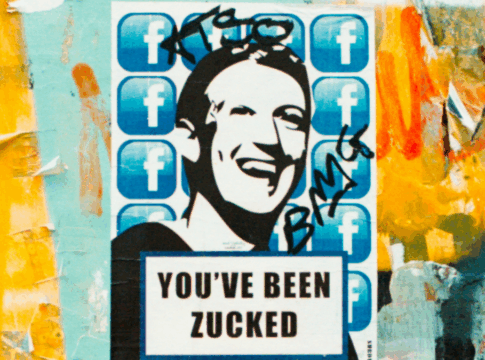 Em um parede com grafites, há um poster com uma ilustração do rosto de Mark Zuckenberg, CEO da Meta, com a seguinte frase em inglês: 