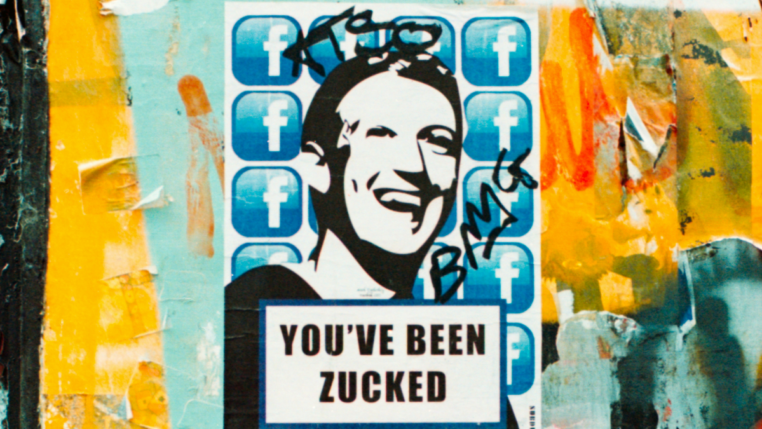 Em um parede com grafites, há um poster com uma ilustração do rosto de Mark Zuckenberg, CEO da Meta, com a seguinte frase em inglês: "Você foi Zuckeado"