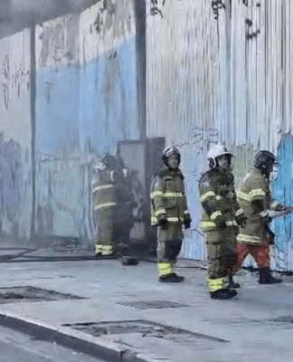 Um grupo de cinco bombeiros, devidamente paramentados, entram no galpão que abrigava equipamentos de quatro escolas de samba no Rio de Janeiro