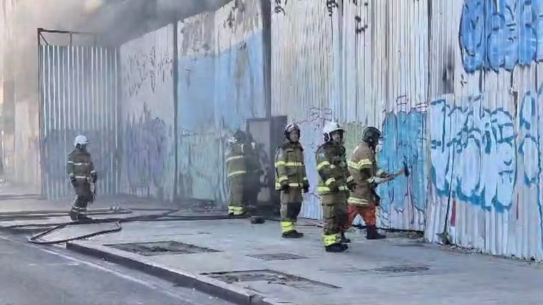 Um grupo de cinco bombeiros, devidamente paramentados, entram no galpão que abrigava equipamentos de quatro escolas de samba no Rio de Janeiro