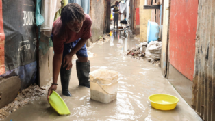 Mulher usa bacia para colher água do chão alagado numa rua estreia