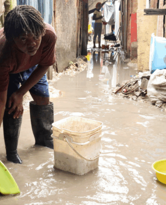 Mulher usa bacia para colher água do chão alagado numa rua estreia