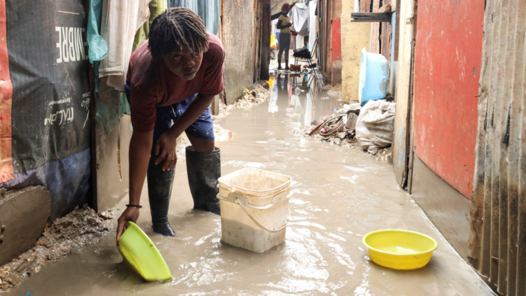 Mulher usa bacia para colher água do chão alagado numa rua estreia