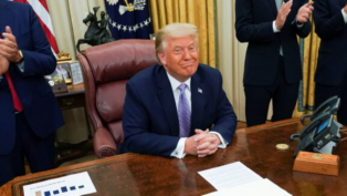 Donald Trump sentado à sua mesa na Casa Branca e sorrindo