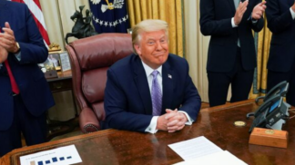 Donald Trump sentado à sua mesa na Casa Branca e sorrindo