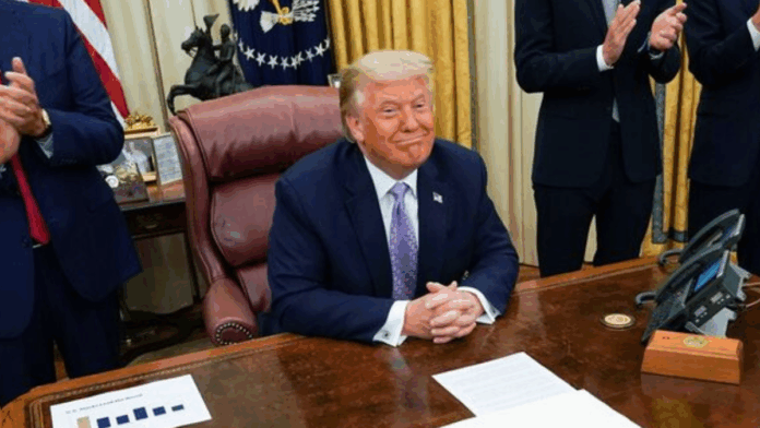 Donald Trump sentado à sua mesa na Casa Branca e sorrindo