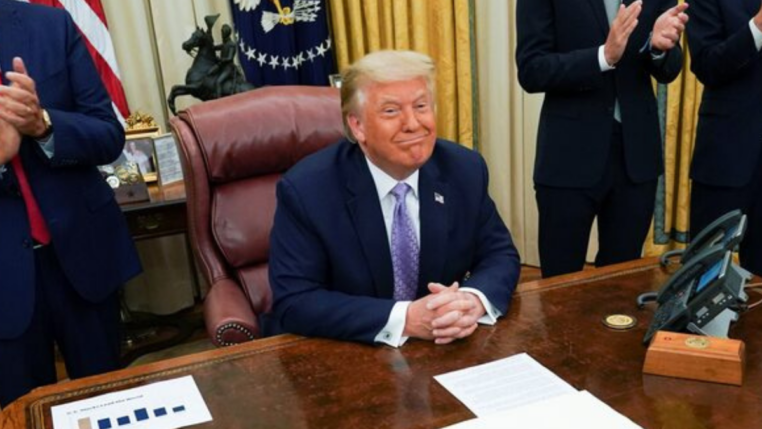 Donald Trump sentado à sua mesa na Casa Branca e sorrindo