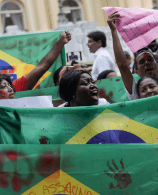 Pessoas erguem bandeiras do Brasil com marcas de mãos pintadas de vermelho em protesto