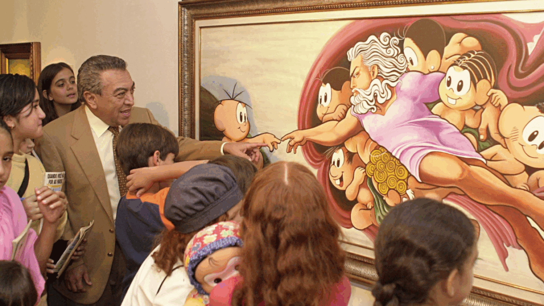 Homem de terno bege e gravata clara, cercado por várias crianças, observa e interage com uma pintura colorida emoldurada. A obra é uma releitura bem-humorada da criação de Adão, de Michelangelo, com personagens infantis de desenho animado no lugar das figuras originais. Algumas crianças apontam para o quadro e uma delas segura um boneco. A cena transmite um ambiente educativo e alegre em uma exposição de arte.