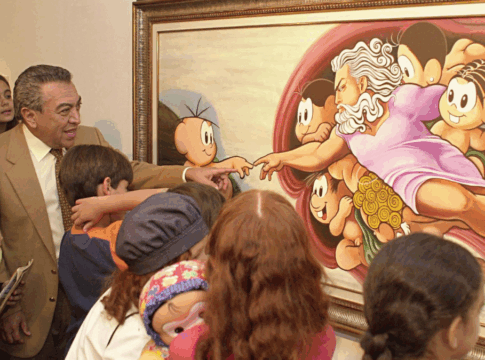 Homem de terno bege e gravata clara, cercado por várias crianças, observa e interage com uma pintura colorida emoldurada. A obra é uma releitura bem-humorada da criação de Adão, de Michelangelo, com personagens infantis de desenho animado no lugar das figuras originais. Algumas crianças apontam para o quadro e uma delas segura um boneco. A cena transmite um ambiente educativo e alegre em uma exposição de arte.