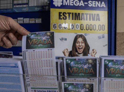 Pessoa segura um volante da “Mega da Virada” em uma casa lotérica. Ao fundo, um cartaz da Mega-Sena exibe a estimativa de prêmio de 600 milhões de reais e a imagem de uma mulher sorridente comemorando.