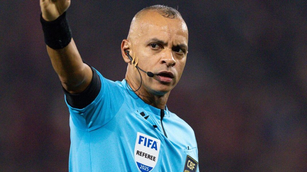 Árbitro Wilton Pereira Sampaio, com o braço direito aberto, uniforme azul FIFA.