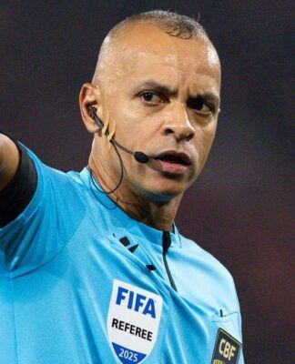 Árbitro Wilton Pereira Sampaio, com o braço direito aberto, uniforme azul FIFA.