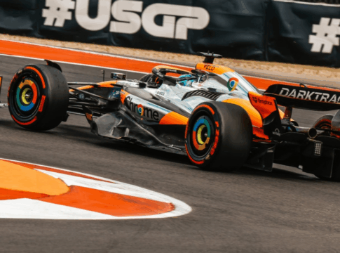 Carro de Fórmula 1 da Mclaren, laranja e prata, fazendo uma curva à esquerda.