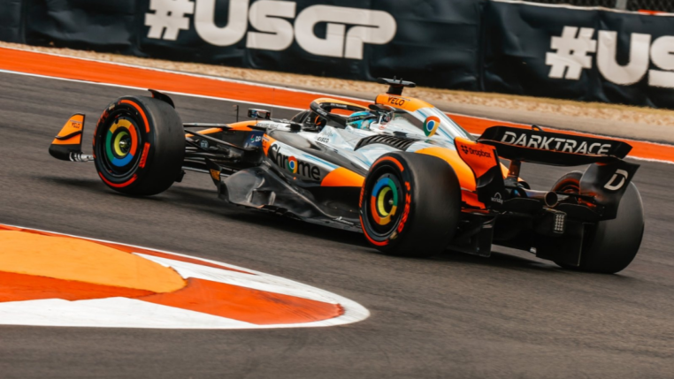 Carro de Fórmula 1 da Mclaren, laranja e prata, fazendo uma curva à esquerda.