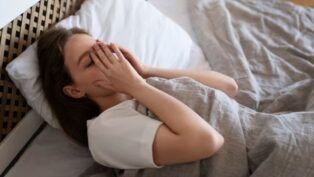 Mulher cansada deitada na cama com a mão no rosto