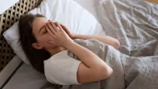 Mulher cansada deitada na cama com a mão no rosto