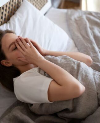 Mulher cansada deitada na cama com a mão no rosto