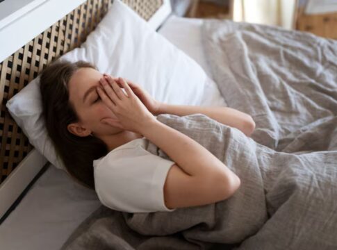 Mulher cansada deitada na cama com a mão no rosto