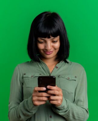 Mulher de cabelo preto com franja em um fundo verde segurando um celular