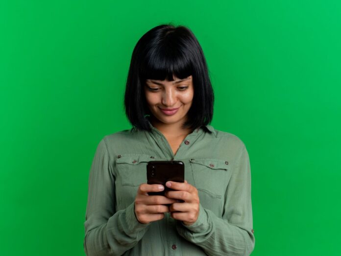 Mulher de cabelo preto com franja em um fundo verde segurando um celular