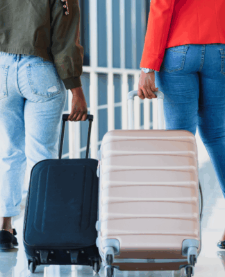 Duas mulheres caminham pelo aeroporto, cada uma puxando sua mala.