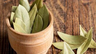 A imagem mostra um pote em cima de uma mesa de madeira cheio de folhas de louro