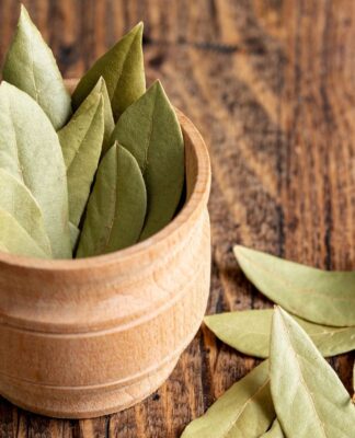 A imagem mostra um pote em cima de uma mesa de madeira cheio de folhas de louro