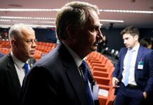 Imagem mostra o ex-presidente Jair Bolsonaro em audiência do julgamento da tentativa de golpe. Ele aparece no primeiro plano, com uma sombra que deixa apenas a silhueta do rosto dele. Atrás aparecem cadeiras da audiência.