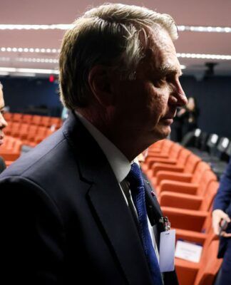 Imagem mostra o ex-presidente Jair Bolsonaro em audiência do julgamento da tentativa de golpe. Ele aparece no primeiro plano, com uma sombra que deixa apenas a silhueta do rosto dele. Atrás aparecem cadeiras da audiência.